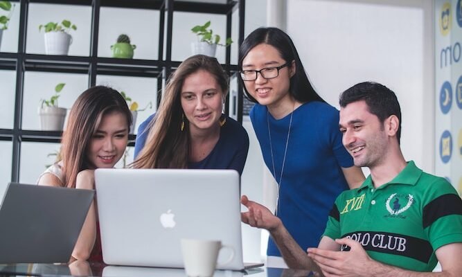 four people watching on white MacBook on top of glass-top table