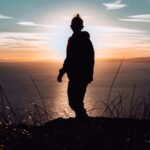 silhouette of man standing on hill during sunset